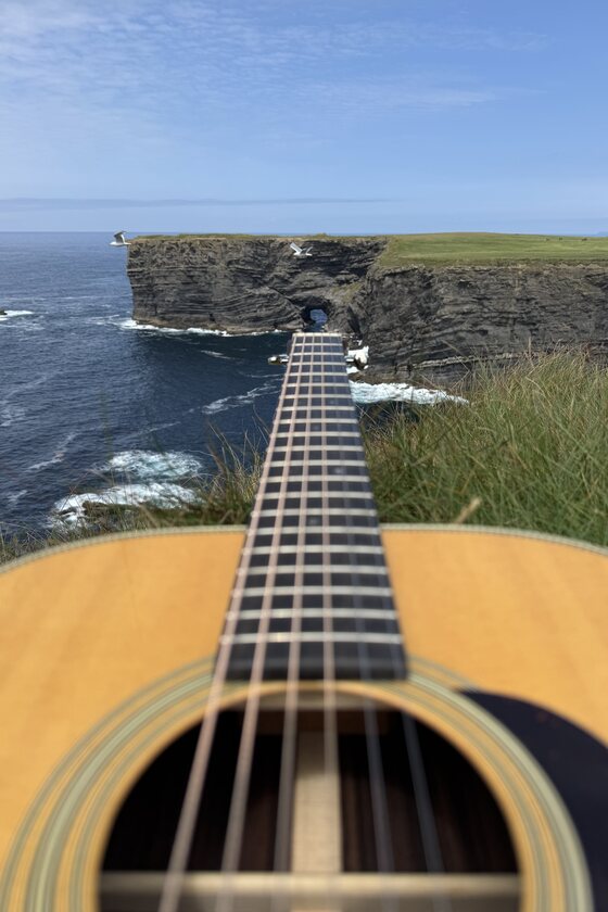 The neck of a guitar pointing out over sea cliffs and open water
